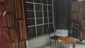 A room with a wooden door, a window with white frames, a chair, a table, and a tiled floor. - Vijiji Hotel and Conference Eldoret (Eldoret)