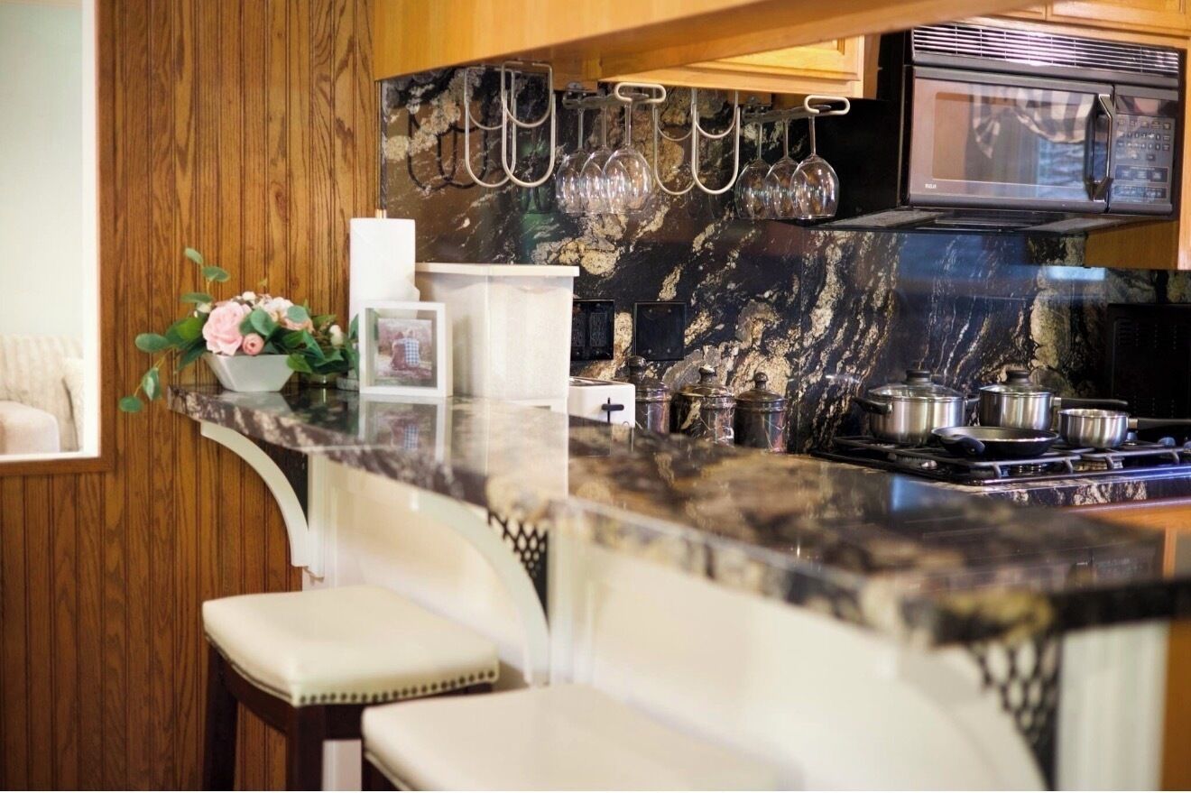 A kitchen with a marble countertop, a microwave, and hanging wine glasses.