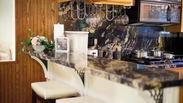 A kitchen with a marble countertop, a microwave, and hanging wine glasses.