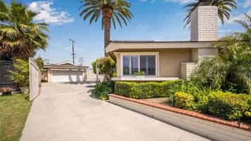 A single-story house with a garage, a brick chimney, and a well-maintained front yard with palm trees and shrubs.