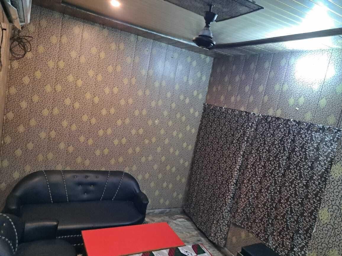 Habitació amb paper pintat, un sofà de cuir negre, una carpeta vermella i un ventilador de sostre.