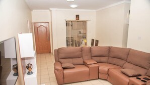 A living room with a brown sectional sofa, a white TV stand, and a fur rug. - Regimanuel Estates  (Kwabenya)