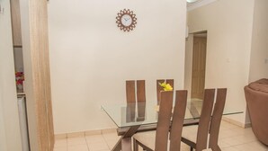 A dining area with a glass table and wooden chairs, a clock on the wall, and a door in the background. - Regimanuel Estates  (Kwabenya)