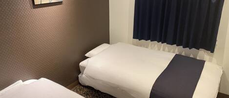 A small, single-bed room with a patterned carpet, a dark blue curtain, and a framed picture on the wall.