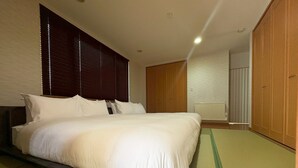 A neatly made bed in a hotel room with a large window, a radiator, and wooden wardrobes. - BAY LUNA (Hakodate)
