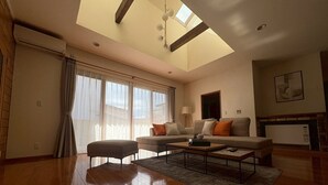 A spacious living room with a high ceiling, a sofa set, a coffee table, and a fireplace. - BAY LUNA (Hakodate)