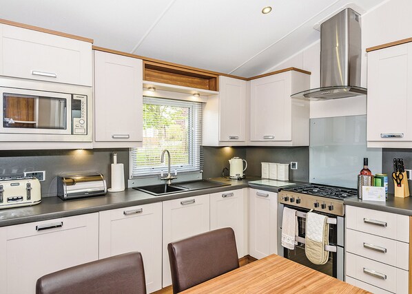 A compact kitchen with a microwave, toaster, sink, stove, and dining area with chairs.