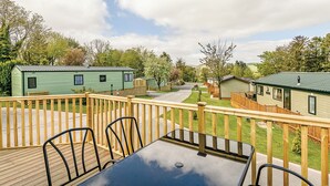 Una terraza con mesa y sillas, rodeada por una valla de madera, con vistas a una hilera de casas móviles con techos verdes.
