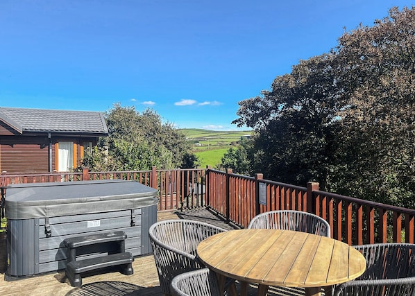 A deck with outdoor seating, a hot tub, and a view of a green landscape.