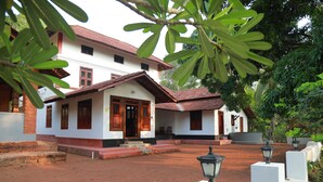 A traditional house with a tiled roof, a porch, and a garden area with a lamp post. - Vilayara Heritage Retreat (Kozhikode)