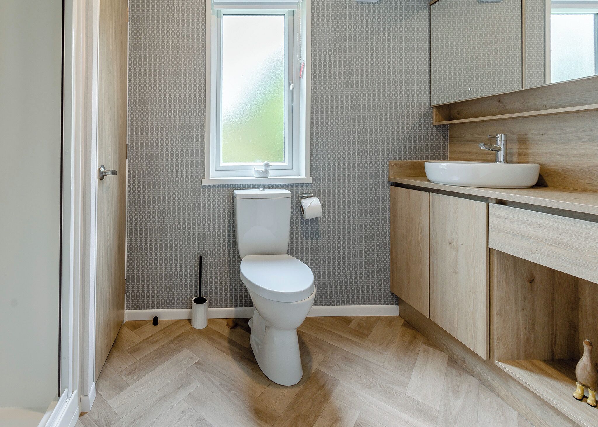 A bathroom with a toilet, a window, a sink, and wooden cabinetry.