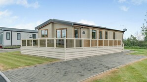 A single-story mobile home with a fenced deck, a satellite dish, and a paved driveway.