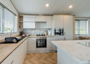Une cuisine compacte équipée d’un évier, d’une cuisinière, d’un four, d’un four à micro-ondes et d’un plan de travail en marbre.