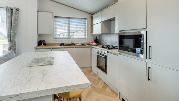 A modern kitchen with a marble island, stainless steel appliances, and a window with blinds.