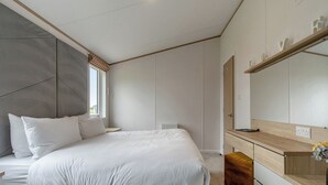 A bedroom with a bed, a bedside table, a dresser, a mirror, and a radiator.