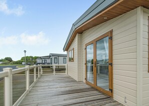 Un bâtiment moderne doté d’une terrasse en bois, de grandes portes-fenêtres coulissantes et offrant une vue sur d’autres constructions similaires à l’arrière-plan.