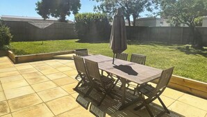 Een terras met een tafel en stoelen, omgeven door een gazon en een houten hek.