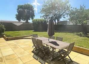 A patio with a table and chairs, surrounded by a grassy yard and a wooden fence.