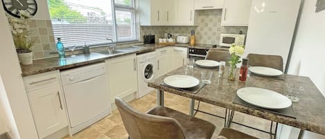 Une cuisine moderne avec des armoires blanches, un four encastré, un four à micro-ondes et un coin repas avec une table dressée pour deux personnes.