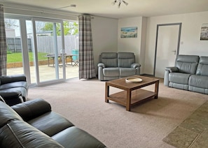 A living room with a sofa, two armchairs, a coffee table, and a sliding glass door leading to a patio.