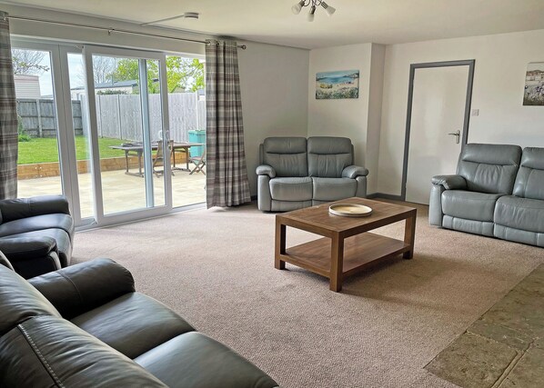 Een woonkamer met een bank, twee fauteuils, een salontafel en een schuifdeur die uitkomt op een terras.