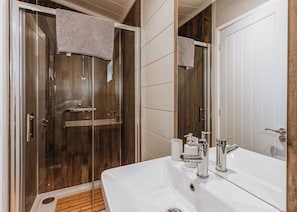 Een badkamer met een glazen douchecabine, een witte wastafel met chroomkranen en een houten vloer.
