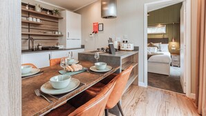 Une cuisine moderne avec un coin repas, un four encastré et une vue sur une chambre à coucher équipée d’un lit et d’une table de chevet.