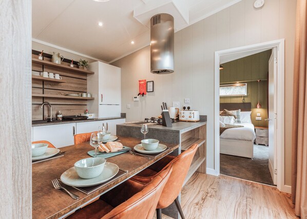 Une cuisine moderne avec un coin repas, un four encastré et une vue sur une chambre à coucher équipée d’un lit et d’une table de chevet.