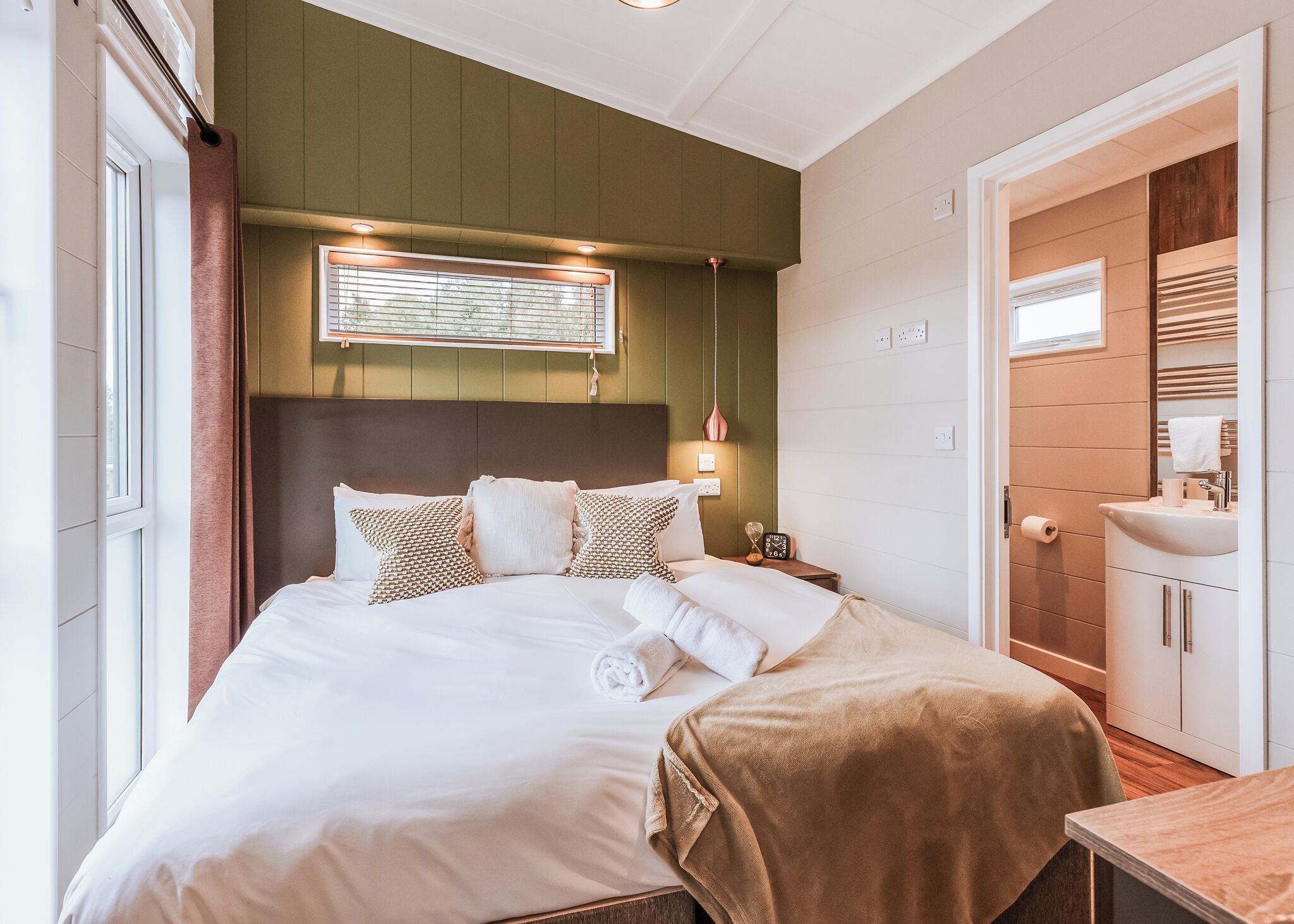 A neatly arranged bedroom with a bed, bedside table, and a bathroom with a sink and mirror.