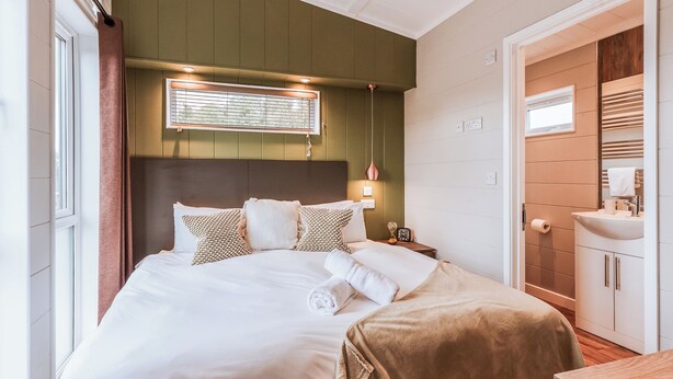 A neatly arranged bedroom with a bed, bedside table, and a bathroom with a sink and mirror. - Magnolia Lodge VIP Hot Tub (Bridgnorth)