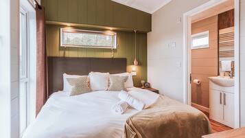 A neatly arranged bedroom with a bed, bedside table, and a bathroom with a sink and mirror.