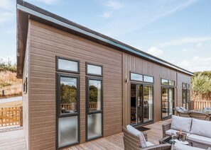 A modern building with large windows, a deck with outdoor furniture, and a wooden exterior.