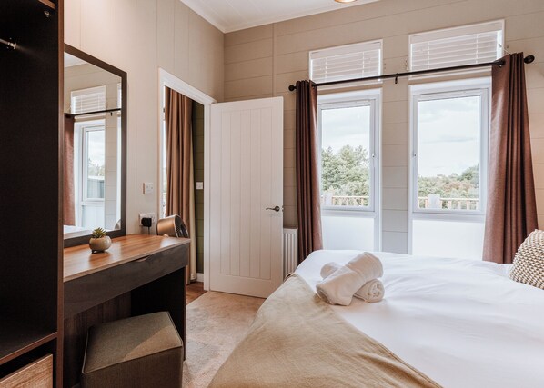 A hotel room with a bed, a bedside table, a mirror, a window with curtains, and a view of the outdoors.