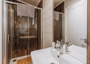 A bathroom with a glass shower enclosure, a white sink with chrome fixtures, and a wooden floor.
