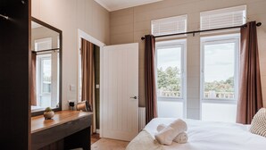 Une chambre d’hôtel comprenant un lit, une table de chevet, un miroir, une fenêtre avec des rideaux et une vue sur l’extérieur.