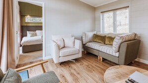 A room with a bed, a sofa, a chair, a table, and a window with blinds. - Magnolia Lodge VIP Hot Tub (Bridgnorth)