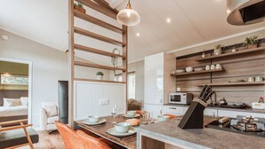 Une cuisine moderne dotée d’un îlot central, d’étagères en bois et d’un coin repas avec des chaises orange.