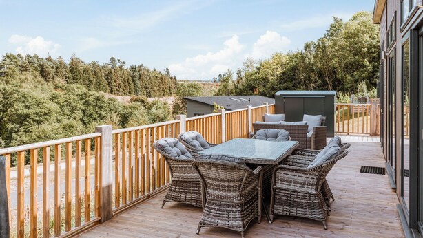 Un balcon doté de meubles en osier, d’une table et offrant une vue sur les arbres et les collines.