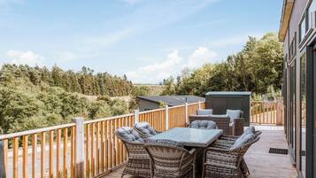 A balcony with wicker furniture, a table, and a view of trees and hills.