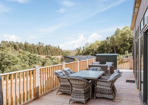 Een balkon met rieten meubels, een tafel en uitzicht op bomen en heuvels.