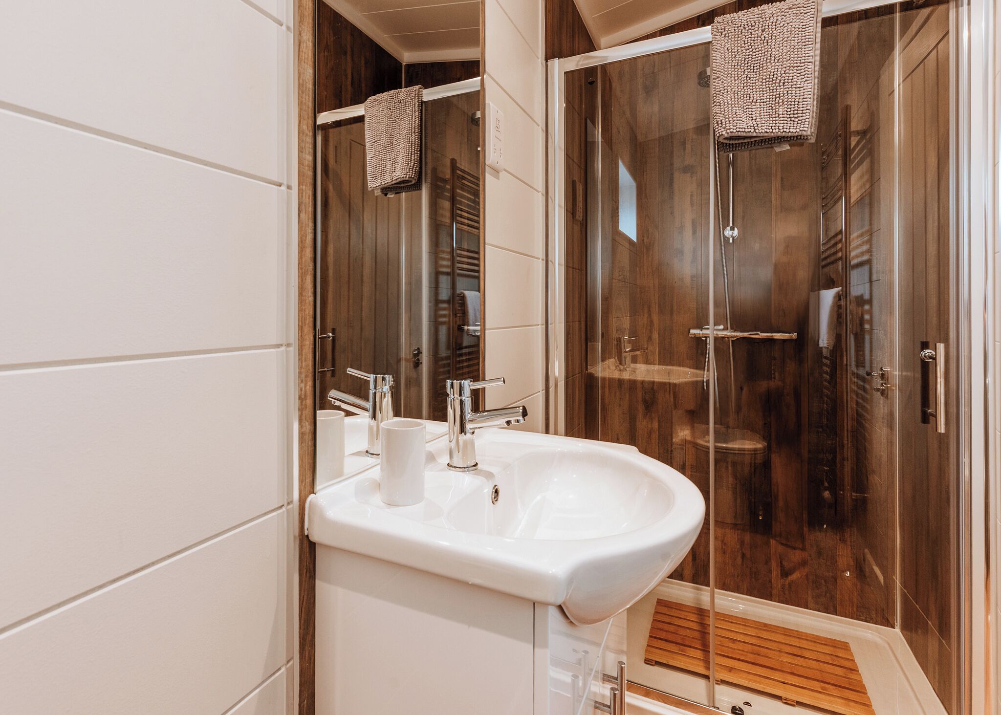 A bathroom with a white sink, two mirrors, and a glass-enclosed shower.