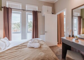 Een slaapkamer met een bed, een dressoir, een spiegel en een raam met gordijnen.