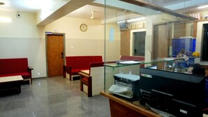 A waiting area with a reception desk, a clock, and a glass partition. - Kamala Shanti Palace (Solapur)