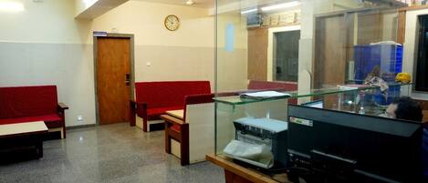 A waiting area with a reception desk, a clock, and a glass partition.