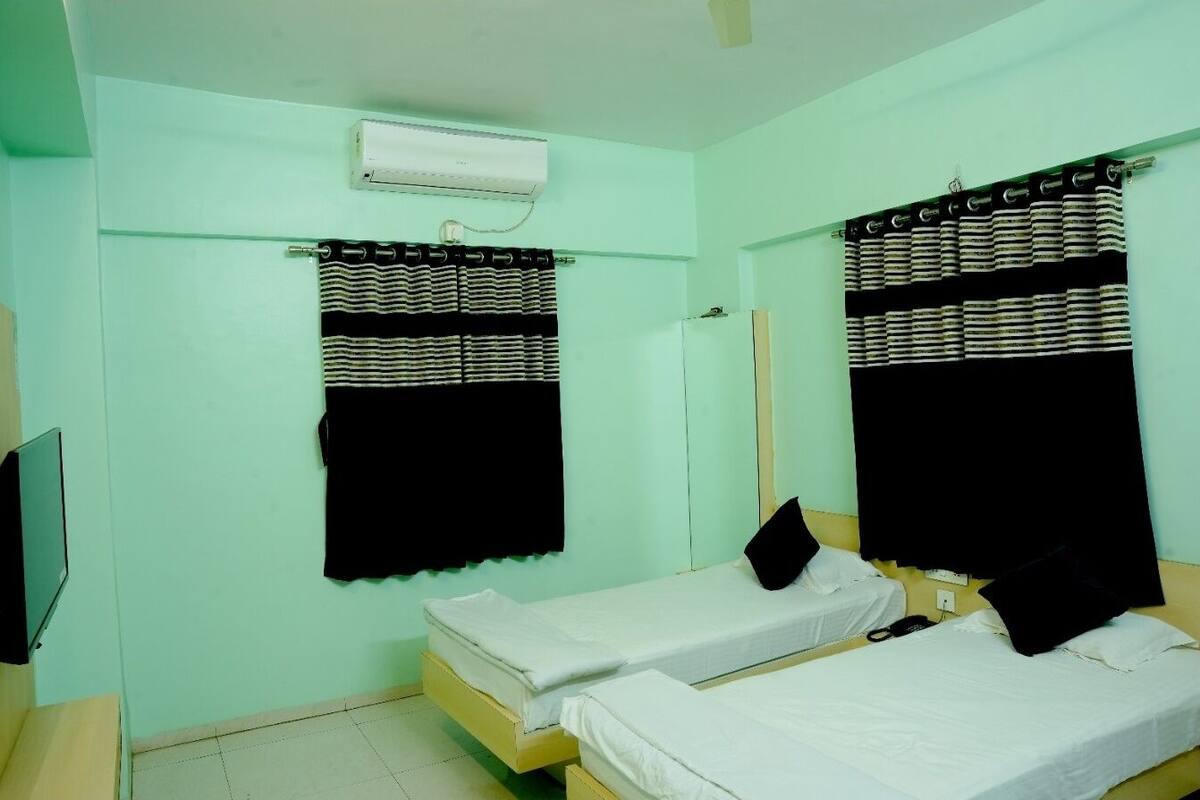 Una habitación con dos camas individuales, un televisor de pantalla plana, aire acondicionado y una ventana con cortinas a rayas.