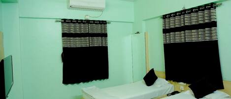 A room with two single beds, a flat-screen TV, an air conditioning unit, and a window with striped curtains.