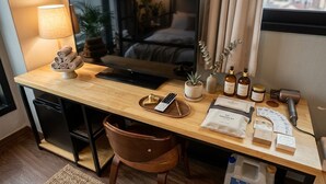 Une chambre d’hôtel avec un bureau en bois, une télévision, une lampe, une plante et une vue sur la ville.