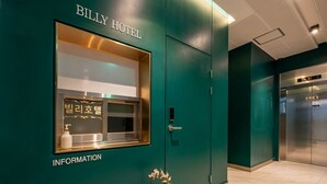L’entrée d’un hôtel, avec un mur végétal, un comptoir d’accueil et un ascenseur.