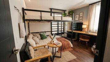 A compact studio apartment with bunk beds, a desk, a chair, a sofa, and a small round table.