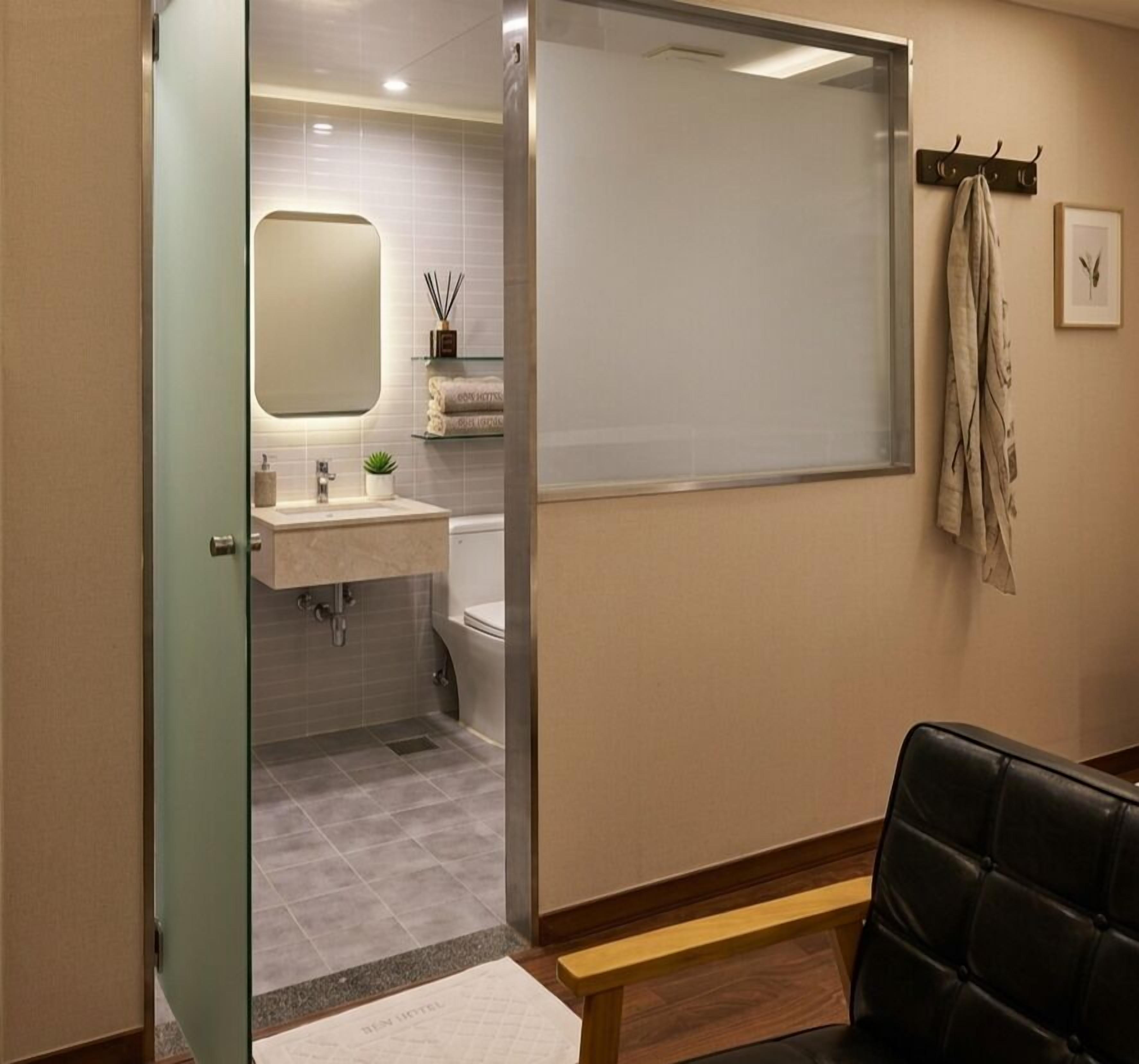 Baño de hotel con mampara de vidrio, lavamanos, inodoro y espejo.